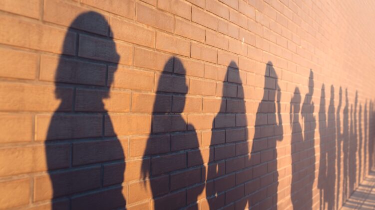 a line of shadows of people lined up against a red brick wall. Stand in a queue to the changes.