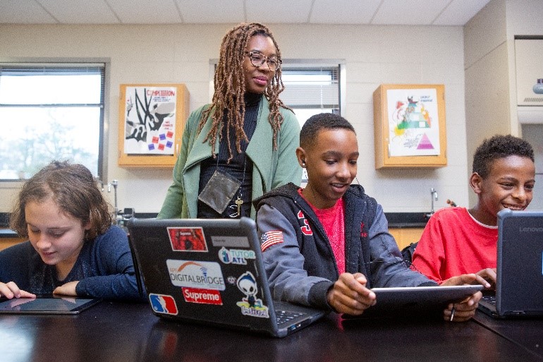 teacher standing behind students on their laptops