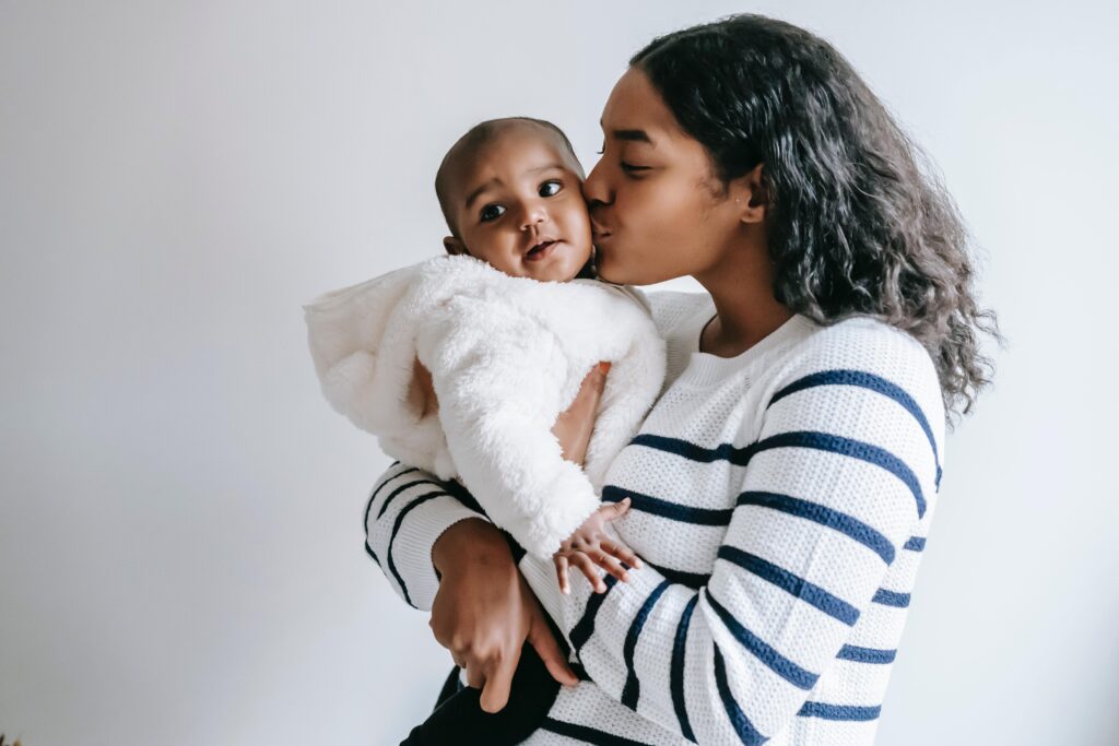 Black mother in striped shirt holding Black baby in fluffy white coat.