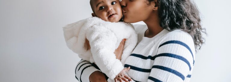 Black mother in striped shirt holding Black baby in fluffy white coat.