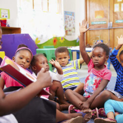 Class of preschool children raising hands to answer teacher