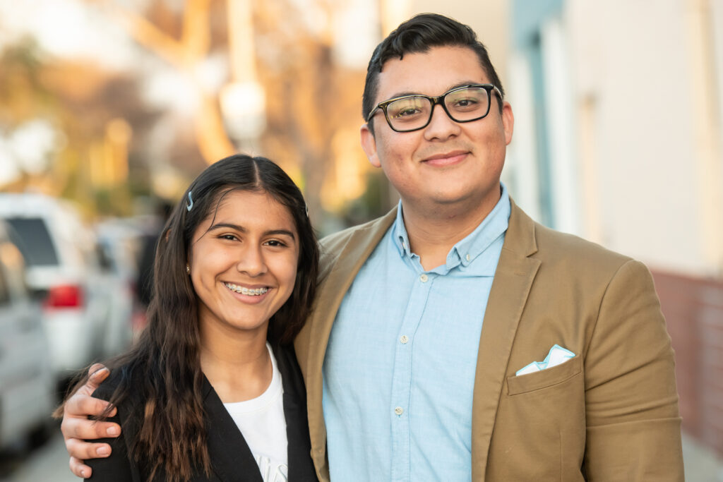 Smiling Hispanic young man posing with his sister looking at the camera.