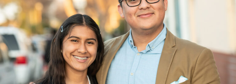 Smiling Hispanic young man posing with his sister looking at the camera.