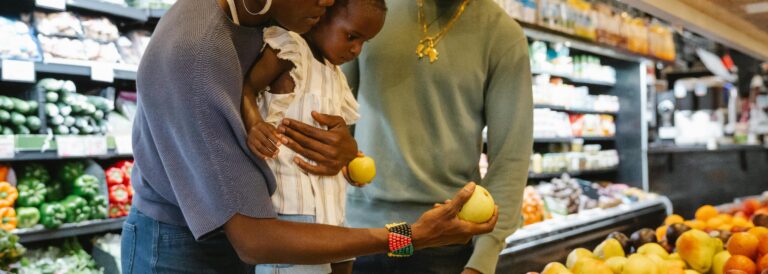Photo of two Black parents and their child selecting produce at a grocery store