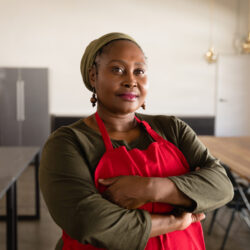 a Black woman in a red apron looks directly at camera