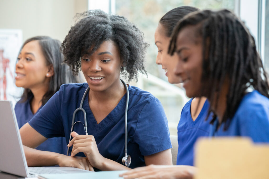 Black nurse uses laptop with colleagues